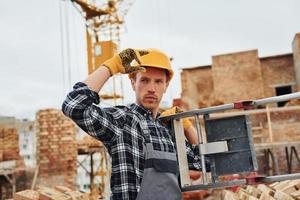 Ladder in hands. Construction worker in uniform and safety equipment have job on building photo
