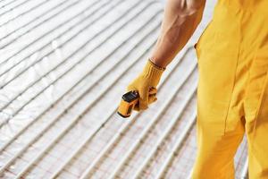 Close up view. Worker in yellow colored uniform installing underfloor heating system photo