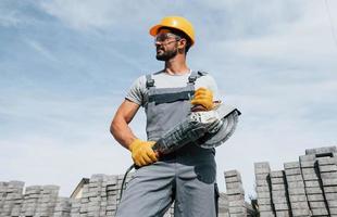 Posing for a camera with circular saw. Male worker in yellow colored uniform have job with pavement photo