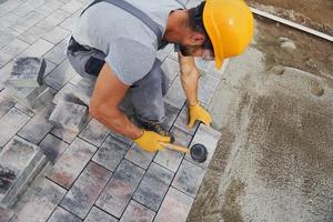 Uses a rubber hammer. Male worker in yellow colored uniform have job with pavement photo