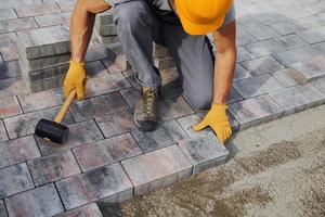 Uses a rubber hammer. Male worker in yellow colored uniform have job with pavement photo