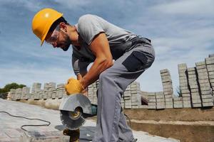 Slicing by circular saw. Male worker in yellow colored uniform have job with pavement photo