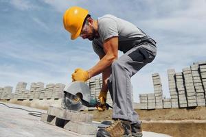 Slicing by circular saw. Male worker in yellow colored uniform have job with pavement photo