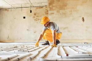 Worker in yellow colored uniform installing underfloor heating system photo