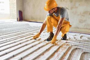 Worker in yellow colored uniform installing underfloor heating system photo