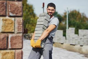 Holds bricks. Male worker in yellow colored uniform have job with pavement photo