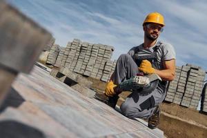 Slicing by circular saw. Male worker in yellow colored uniform have job with pavement photo