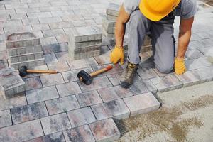 Uses a rubber hammer. Male worker in yellow colored uniform have job with pavement photo