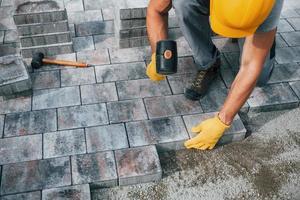 Uses a rubber hammer. Male worker in yellow colored uniform have job with pavement photo