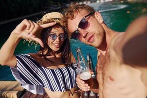 Holding drinks in hands. Cheerful couple or friends together in swimming pool at vacation photo