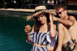 Holding drinks in hands. Cheerful couple or friends together in swimming pool at vacation photo