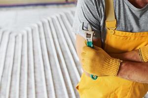 Close up view. Worker in yellow colored uniform installing underfloor heating system photo