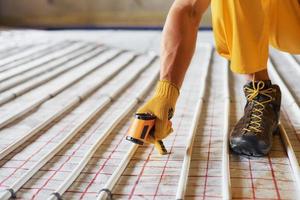 Measures heat of the pipes. Worker in yellow colored uniform installing underfloor heating system photo