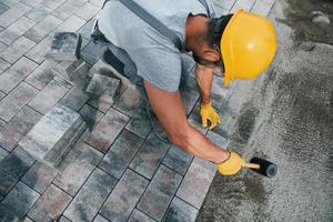 utiliza un martillo de goma. trabajador masculino con uniforme de color amarillo tiene trabajo con pavimento foto