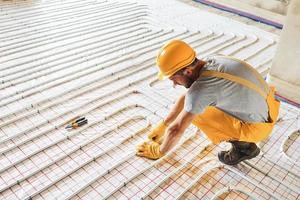 Worker in yellow colored uniform installing underfloor heating system photo