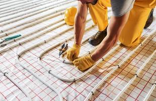 Many of pipes. Worker in yellow colored uniform installing underfloor heating system photo