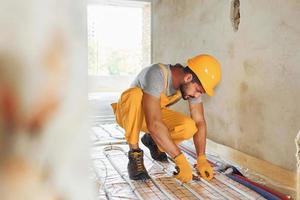 Almost done. Worker in yellow colored uniform installing underfloor heating system photo