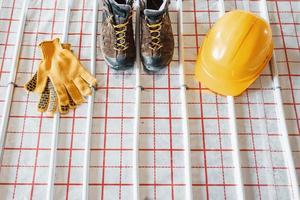 Shoes, hard hat and gloves. Pipes of underfloor heating system. Close up view. No people photo