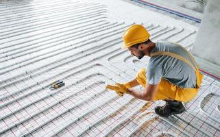 Worker in yellow colored uniform installing underfloor heating system photo
