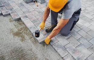 Uses a rubber hammer. Male worker in yellow colored uniform have job with pavement photo