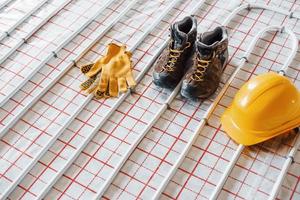 Shoes, hard hat and gloves. Pipes of underfloor heating system. Close up view. No people photo