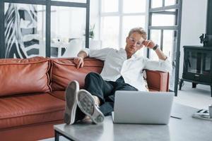 With laptop. Caucasian young guy in elegant white shirt indoors at home photo