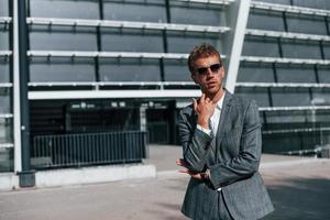 joven empresario exitoso en ropa formal gris está al aire libre en la ciudad foto