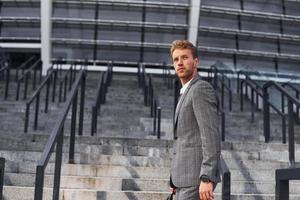 joven empresario exitoso en ropa formal gris está al aire libre en la ciudad foto