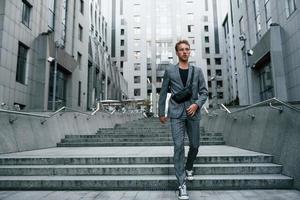 Laptop in hands. Young elegant man in good clothes is outdoors in the city at daytime photo