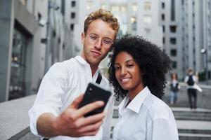 con el teléfono en las manos. hombre con mujer afroamericana juntos en la ciudad al aire libre foto