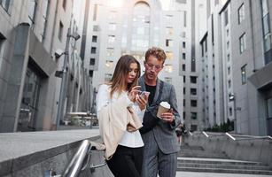 con teléfono y bebida. mujer y hombre en la ciudad durante el día. gente bien vestida foto