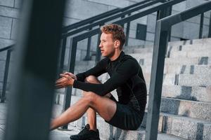 Takes a break. Young man in sportive clothes have workout outdoors at daytime photo