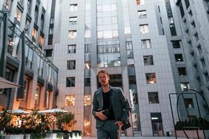 Young elegant man in good clothes is outdoors in the city at daytime photo