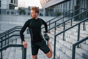 estirar y preparar. un joven con ropa deportiva hace ejercicio al aire libre durante el día foto