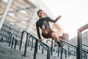 Does parkour. Young man in sportive clothes have workout outdoors at daytime photo