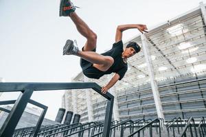 Does parkour. Young man in sportive clothes have workout outdoors at daytime photo