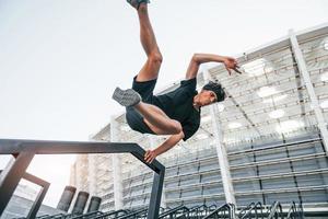 Does parkour. Young man in sportive clothes have workout outdoors at daytime photo