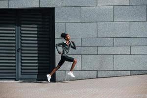 vista lateral de una joven afroamericana con ropa deportiva que corre cerca de la pared foto