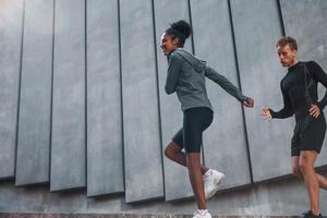 cerca de la gran pared. el hombre europeo y la mujer afroamericana en ropa deportiva hacen ejercicio juntos foto