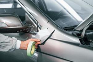 Applying new color. Caucasian automobile repairman in uniform works in garage photo