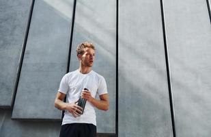 Against building exterior. Young man in sportive clothes have workout outdoors at daytime photo