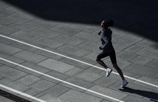 corredor rápido. joven afroamericana con ropa deportiva hace ejercicio al aire libre durante el día foto