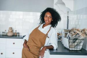 On the kitchen. Young african american woman with curly hair indoors at home photo