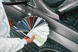 Holds cards with different colors. Caucasian automobile repairman in uniform works in garage photo