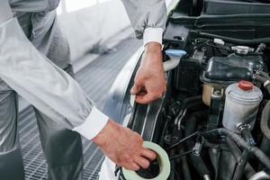 Detailed work. Caucasian automobile repairman in uniform have job in garage photo