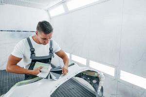 Detailed work. Caucasian automobile repairman in uniform have job in garage photo