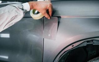 Applying new color. Caucasian automobile repairman in uniform works in garage photo