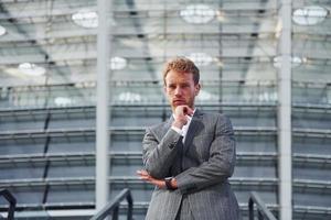 On the stairs of stadium. Young businessman in grey formal wear is outdoors in the city photo