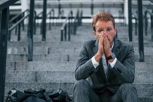 Smoking cigarette. Young businessman in grey formal wear is outdoors in the city photo