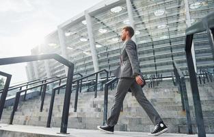 Holds bag in hands. Young businessman in grey formal wear is outdoors in the city photo